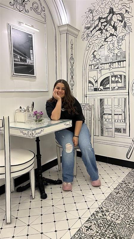 Muskan Mandot, sitting at a café table in front of a hand-drawn mural.